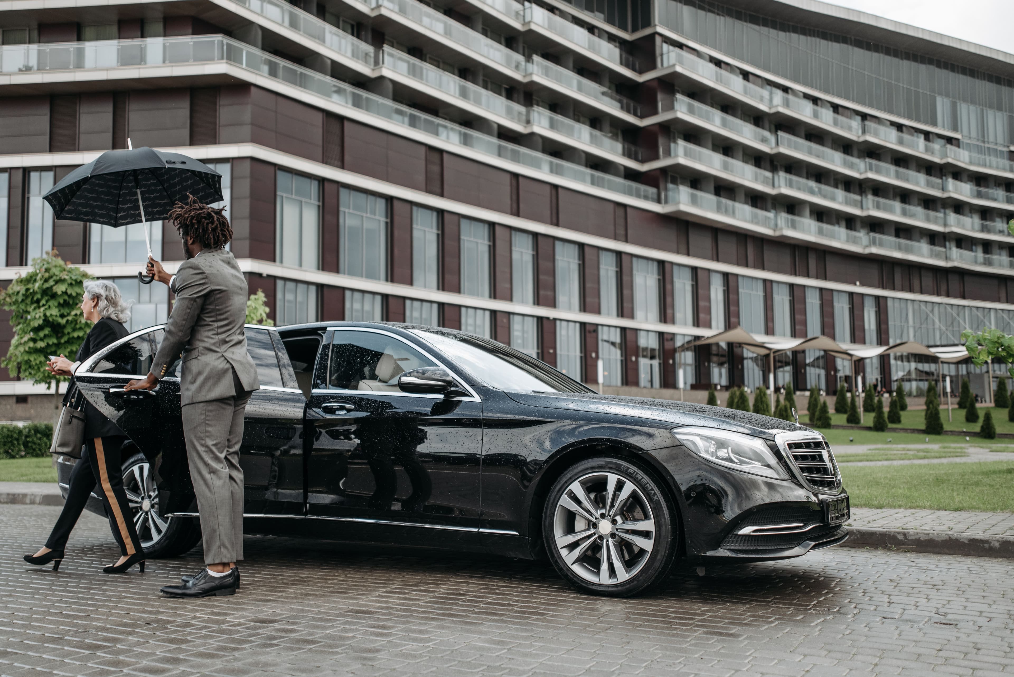 Chauffeur escorting client to the car with an umbrella