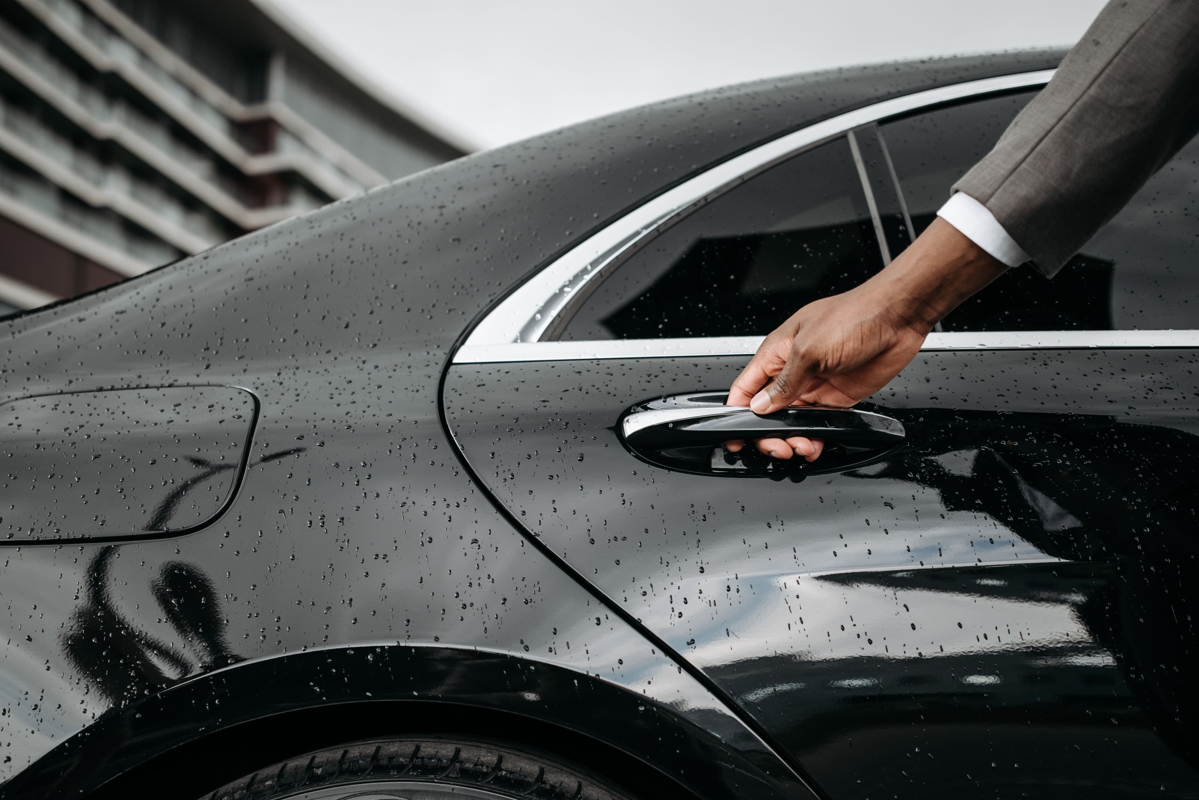 Close-up of a chauffeur opening a car door in the rain